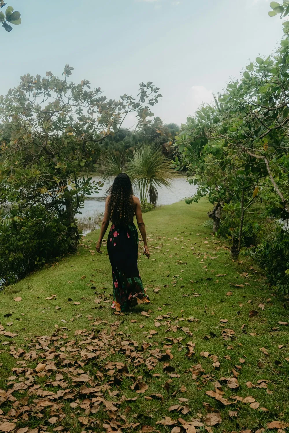A young woman in a long dress walking along a leafy path by the water