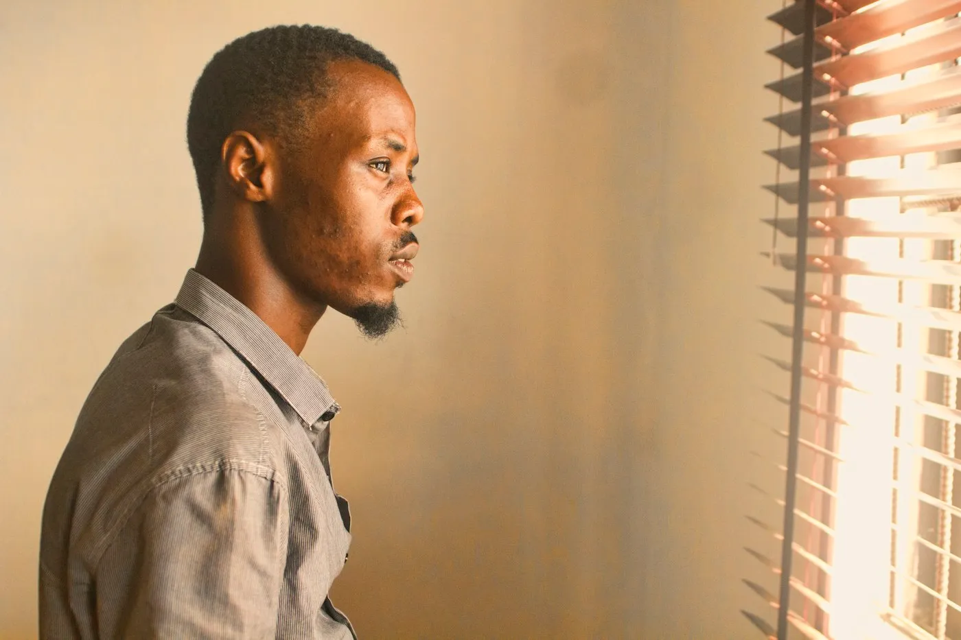 A young man standing by a window in soft light, lost in thought